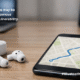 Wireless Bluetooth earbuds on a table next to a smartphone showing a map route, with another device in the background to suggest tracking through a Bluetooth audio vulnerability.